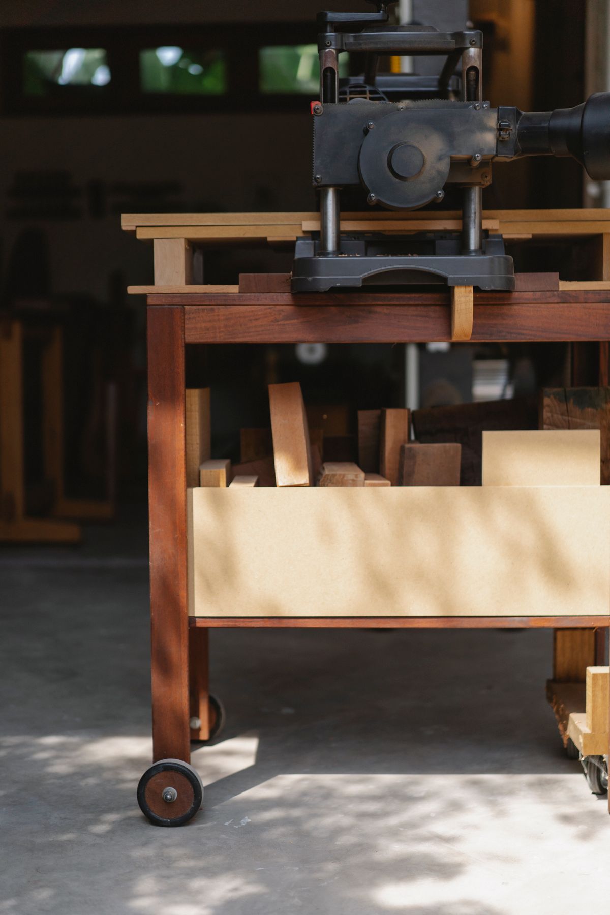 A woodworking machine and timber on a mobile workbench, lit by afternoon sun.